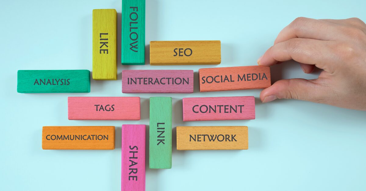 Hand arranging colorful blocks with words like Social Media, SEO, Content, and Interaction — representing key elements of social media management platforms