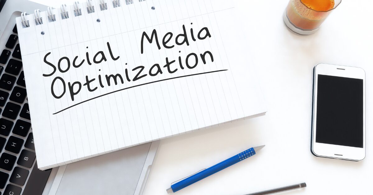 Notebook with 'Social Media Optimization' written on it, placed on a desk with a smartphone, pen, and juice — representing content planning for social platforms